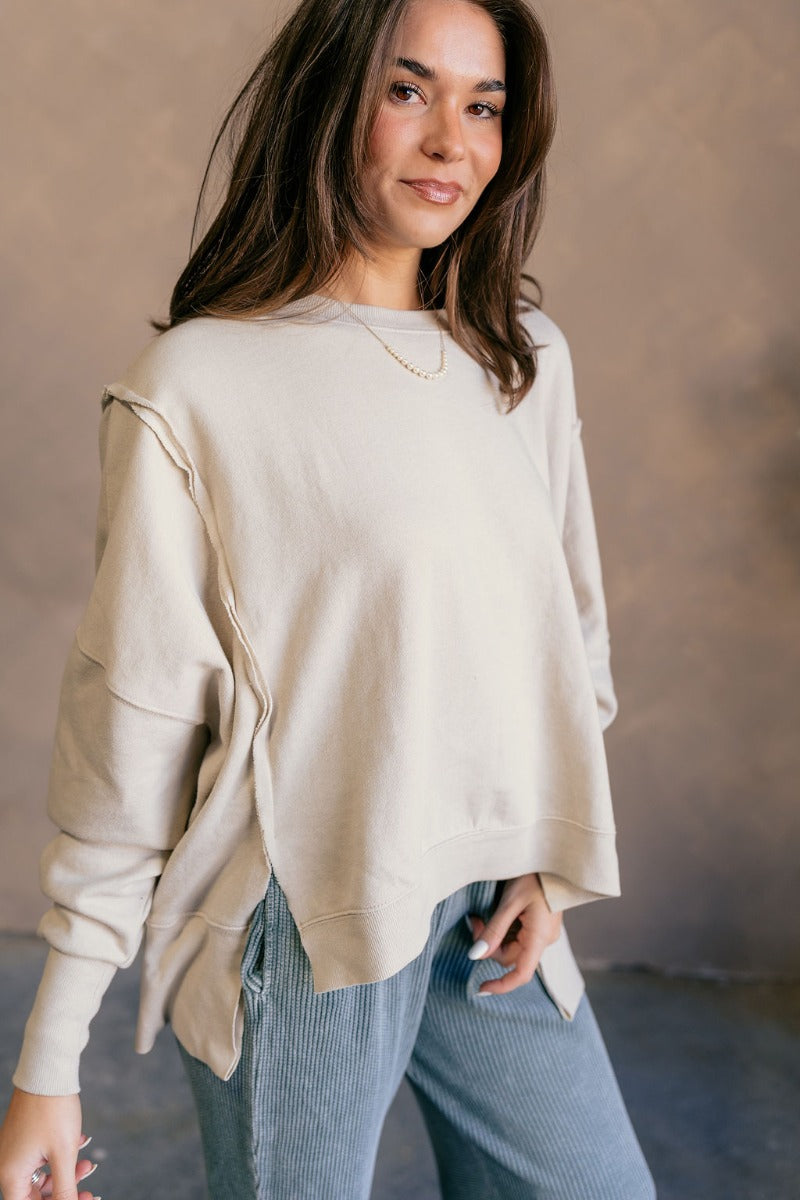 Side view of model wearing the Lyla Cream Long Sleeve Sweatshirt which features washed black knit fabric, a ribbed hem with slight slits on each side, raw hem details, a round ribbed neckline, dropped shoulders and long balloon sleeves with ribbed cuffs.