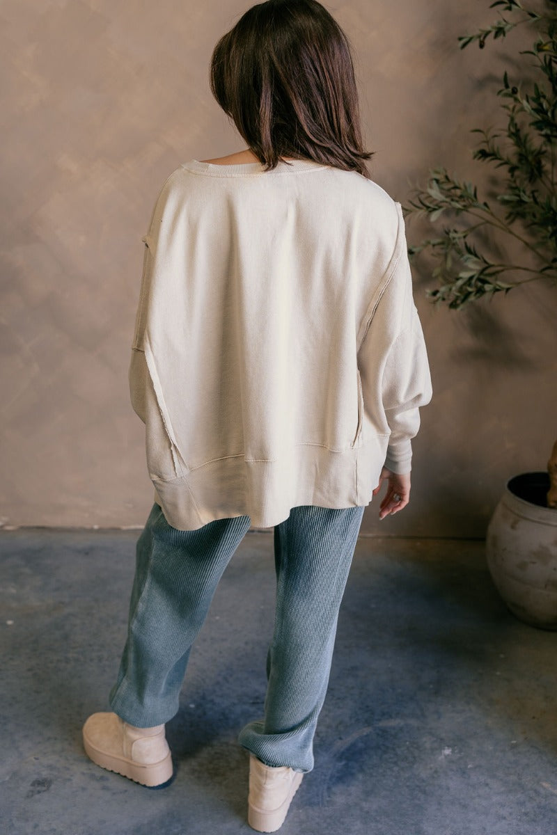 Back view of model wearing the Lyla Cream Long Sleeve Sweatshirt which features washed black knit fabric, a ribbed hem with slight slits on each side, raw hem details, a round ribbed neckline, dropped shoulders and long balloon sleeves with ribbed cuffs.