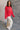 Full body side view of model wearing the Merry Red Ribbed Long Sleeve Sweater which features red and light red ribbed fabric, thick hem, a round neckline, a graphic that says "MERRY" in white outline, dropped shoulders, and long sleeves with ribbed cuffs.