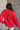 Back view of model wearing the Merry Red Ribbed Long Sleeve Sweater which features red and light red ribbed fabric, thick hem, a round neckline, a graphic that says "MERRY" in white outline, dropped shoulders, and long sleeves with ribbed cuffs.