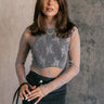  front view of model wearing the Nadia Grey Lace Long Sleeve Top that has grey sheer fabric, lettuce hem details, a lace floral design, a high neckline, and long sleeves. Worn tucked into black skirt over black tank.