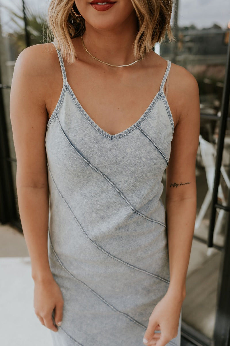 Upper front view of model wearing the Bexley Blue Denim Sleeveless Maxi Dress that has light denim wash fabric, maxi length, a monochrome stitch pattern, a v-neckline, and spaghetti straps.