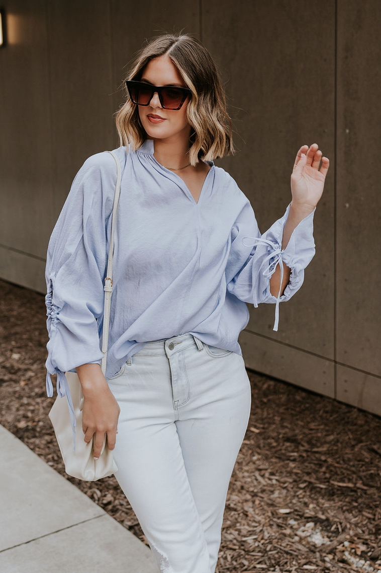 Front view of model wearing the Selene Light Blue Long Sleeve Top which features light blue light weight fabric, v-neckline with collar and long sleeves with an open key hole and cinched details.