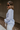 Side view of model wearing the Selene Light Blue Long Sleeve Top which features light blue light weight fabric, v-neckline with collar and long sleeves with an open key hole and cinched details.
