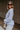 Side view of model wearing the Selene Light Blue Long Sleeve Top which features light blue light weight fabric, v-neckline with collar and long sleeves with an open key hole and cinched details.