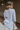 Back view of model wearing the Selene Light Blue Long Sleeve Top which features light blue light weight fabric, v-neckline with collar and long sleeves with an open key hole and cinched details.