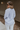 Back view of model wearing the Selene Light Blue Long Sleeve Top which features light blue light weight fabric, v-neckline with collar and long sleeves with an open key hole and cinched details.