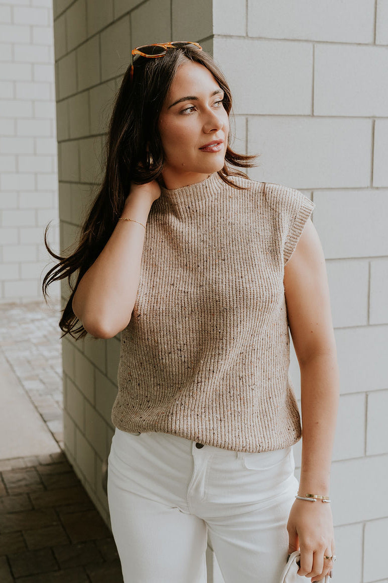 Front view of model wearing the Clara Beige Multi Sleeveless Sweater which features beige cable knit fabric, dark brown and light brown speckled design, ribbed hem, high neckline and sleeveless.
