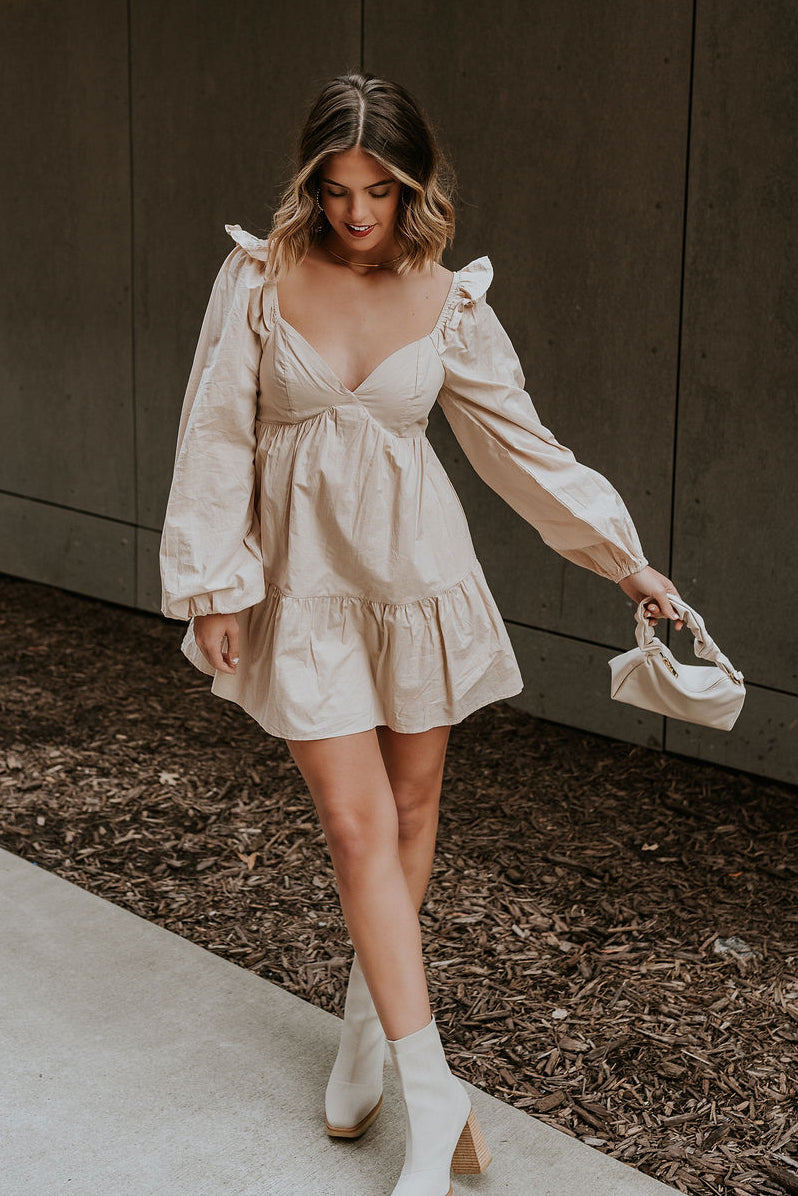 Full body view of model wearing the Stella Beige Long Sleeve Mini Dress which features beige lightweight fabric, mini length, flared skirt, beige lining, sweetheart neckline, ruffle details, long sleeves with elastic wrists and smocked back.