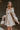 Side view of model wearing the Stella Beige Long Sleeve Mini Dress which features beige lightweight fabric, mini length, flared skirt, beige lining, sweetheart neckline, ruffle details, long sleeves with elastic wrists and smocked back.