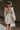 Back view of model wearing the Stella Beige Long Sleeve Mini Dress which features beige lightweight fabric, mini length, flared skirt, beige lining, sweetheart neckline, ruffle details, long sleeves with elastic wrists and smocked back.