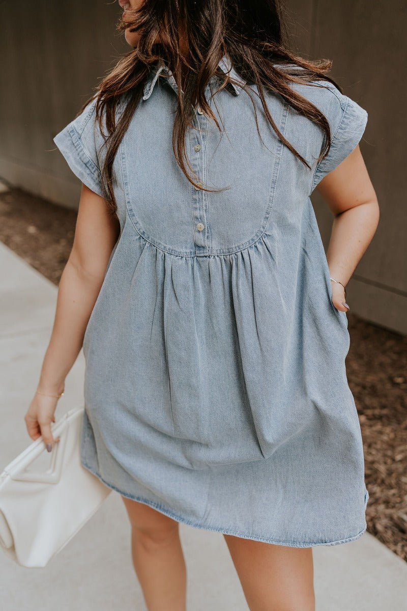 Front view of model wearing the Everly Denim Short Sleeve Buttoned Dress which features light denim wash fabric, mini length, two front slit pockets, quarter pearlescent button up, collared neckline and short sleeves.
