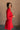 Side view of model wearing the Melina Red Turtleneck Sweater Dress that has red ribbed knit fabric, a flared skirt, mini length, a turtleneck neckline, and long sleeves.