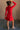 Full body back view of model wearing the Melina Red Turtleneck Sweater Dress that has red ribbed knit fabric, a flared skirt, mini length, a turtleneck neckline, and long sleeves.