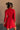 Back view of model wearing the Melina Red Turtleneck Sweater Dress that has red ribbed knit fabric, a flared skirt, mini length, a turtleneck neckline, and long sleeves.