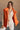 front view of model wearing the Reagan Orange Oversized Puffer Vest that has orange lightweight puffer fabric, a  3 tiered design, orange lining, pockets, a hidden zipper, snaps, a high neck, and a sleeveless design.
