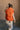 Full body Back view of model wearing the Reagan Orange Oversized Puffer Vest that has orange lightweight puffer fabric, a  3 tiered design, orange lining, pockets, a hidden zipper, snaps, a high neck, and a sleeveless design.