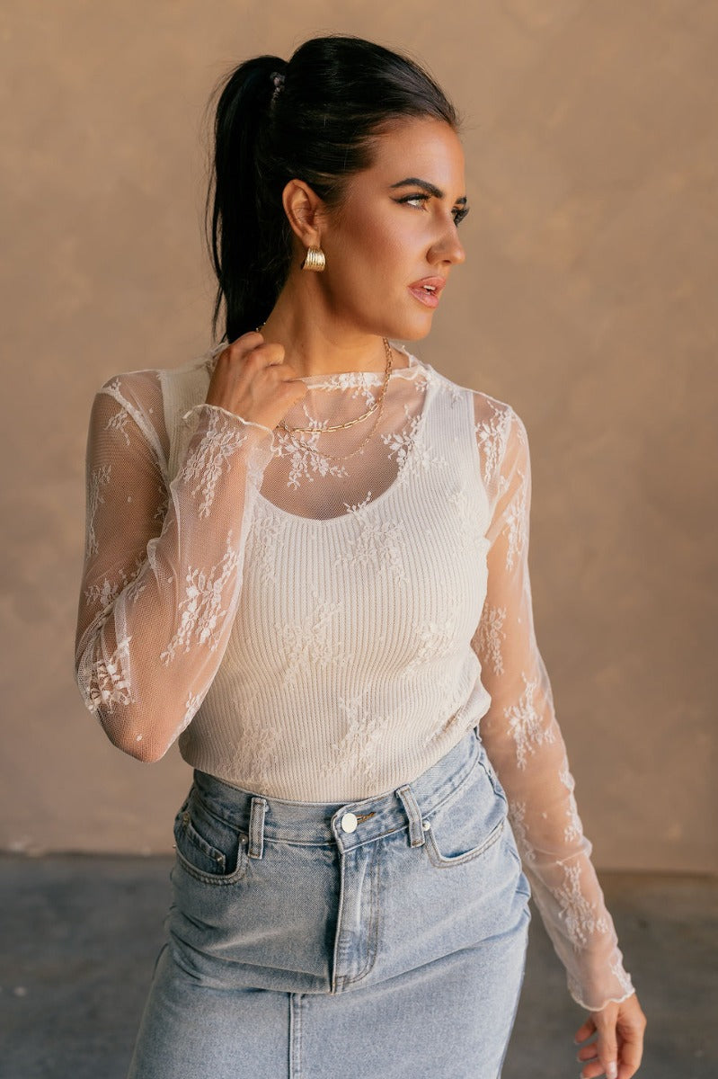 Front view of model wearing the Nadia Cream Lace Long Sleeve Top which features cream sheer fabric, lettuce hem details, lace floral design, high neckline and long sleeves.