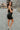Full body side view of model wearing the Brielle Black Sequin Fringe Mini Dress which features black sheer fabric, black lining, mini length, black sequin fringe details, scooped neckline, adjustable straps, sleeveless and monochrome back zippper with hoo