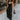 Full body front view of model wearing the Colette Black Floral Satin Midi Dress that has black satin fabric, monochrome florals, a assymetrical ruffle tier design, pleated fabric, a cowl neck, and thin straps.