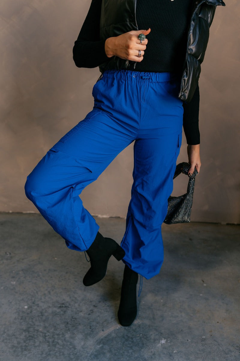 front view of model wearing the Kyla Royal Parachute Cargo Pants that have dark royal breathable nylon fabric, pockets, an elastic waist with a bungee, and relaxed legs with elastic ankles and bungees.