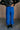 Back view of model wearing the Kyla Royal Parachute Cargo Pants that have dark royal breathable nylon fabric, pockets, an elastic waist with a bungee, and relaxed legs with elastic ankles and bungees.