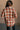 Back view of model wearing the Rowan Rust Multi Plaid Button Up Long Sleeve Top which features rust, brown, beige and grey blue knti fabric, plaid pattern, left front chest pocket, tortoise button up, collared neckline, dropped shoulders and long sleeves 