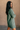 Side view of model wearing the Sasha Grey Green Mock Neck Sweater Dress which features grey green textured knit fabric, a thick ribbed hem, mini length, a high ribbed neckline, and long sleeves with ribbed cuffs.
