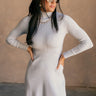 Front view of model wearing the Melina Grey Turtleneck Sweater Dress that has light grey ribbed knit fabric, a flared skirt, mini length, a turtleneck neckline, and long sleeves.