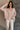Front view of model wearing the Ada Dusty Rose Long Sleeve Top which features dusty mauve pink knit fabric, slight slits on each side, distressed details, a front left chest pocket, a v-neckline with collar, dropped shoulders, and long sleeves with cuffs.