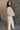 Side view of model wearing the Ada Dusty Rose Long Sleeve Top which features dusty mauve pink knit fabric, slight slits on each side, distressed details, a front left chest pocket, a v-neckline with collar, dropped shoulders, and long sleeves with cuffs.