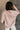 Back view of model wearing the Ada Dusty Rose Long Sleeve Top which features dusty mauve pink knit fabric, slight slits on each side, distressed details, a front left chest pocket, a v-neckline with collar, dropped shoulders, and long sleeves with cuffs.