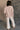 Back view of model wearing the Ada Dusty Rose Long Sleeve Top which features dusty mauve pink knit fabric, slight slits on each side, distressed details, a front left chest pocket, a v-neckline with collar, dropped shoulders, and long sleeves with cuffs.