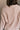 Back view of model wearing the Ada Dusty Rose Long Sleeve Top which features dusty mauve pink knit fabric, slight slits on each side, distressed details, a front left chest pocket, a v-neckline with collar, dropped shoulders, and long sleeves with cuffs.