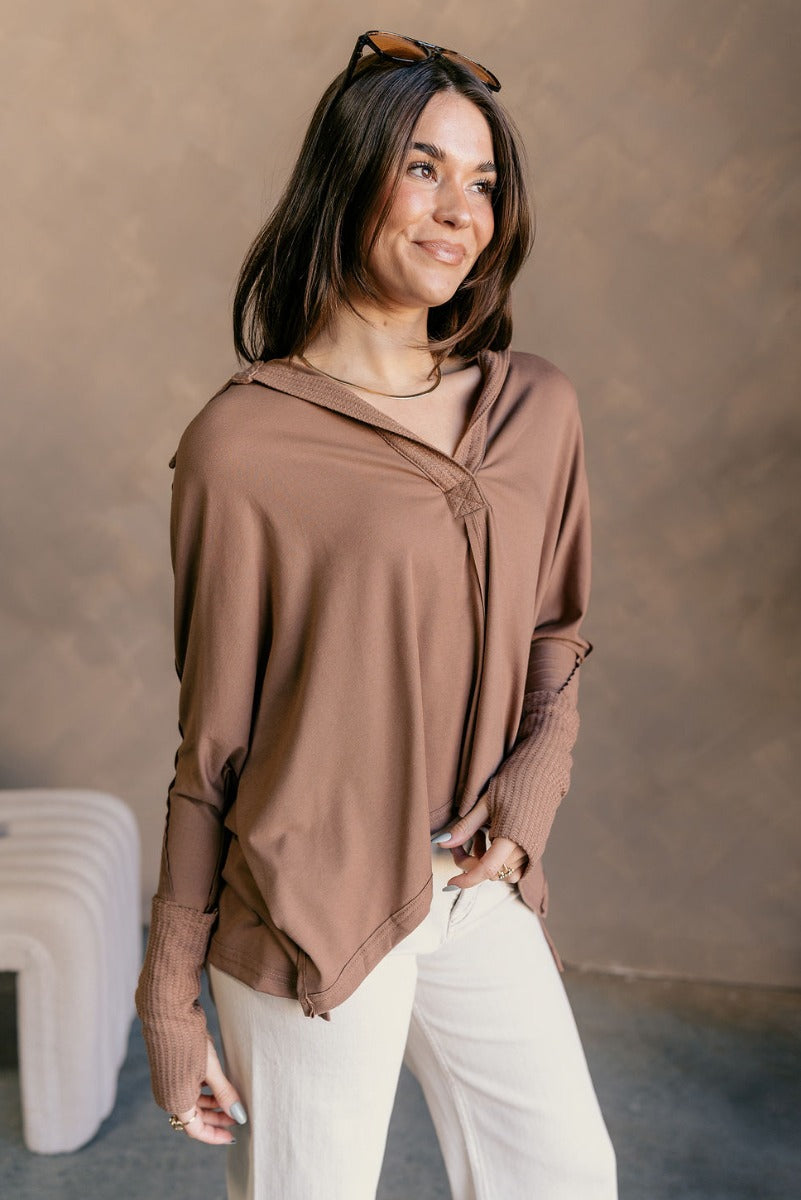 Side view of model wearing the Karlee Mocha Collared Long Sleeve Top which features mocha knit fabric, a high-low hem, slight slits on each side, waffle knit textured details, a v-neckline with a collar, and long sleeves with cuffs.