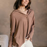 Side view of model wearing the Karlee Mocha Collared Long Sleeve Top which features mocha knit fabric, a high-low hem, slight slits on each side, waffle knit textured details, a v-neckline with a collar, and long sleeves with cuffs.