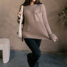 Full body view of model wearing the Mila Mocha Cable Knit Long Sleeve Sweater which features mocha cable knit fabric, a front left chest pocket, a round neckline, dropped shoulders, and long sleeves with folded cuffs.