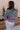 Back view of model wearing the Eliza Purple Multi Long Sleeve Sweater which features purple, peach, cream blue and teal grey knit fabric, a floral and striped pattern, a loose turtle neckline, dropped shoulders, and long balloon sleeves with ribbed cuffs.