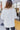 Back view of model wearing the Winter Wonderland Sweater that has white popcorn knit fabric, a v-neckline, dropped shoulders, and long sleeves with ribbed wrists.
