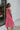 Side view of model wearing the Lost Without You Midi Dress that has a red and pink geometric pattern, a tiered skirt with a midi-length hem, and a draped neck that ties in the back.