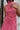Close upper front view of model wearing the Lost Without You Midi Dress that has a red and pink geometric pattern, a tiered skirt with a midi-length hem, and a draped neck that ties in the back.