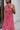 Close front view of model wearing the Lost Without You Midi Dress that has a red and pink geometric pattern, a tiered skirt with a midi-length hem, and a draped neck that ties in the back.