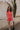 front full body image of modeal wearing The Emily Washed Red Denim Sleeveless Romper features washed red denim fabric, two front pockets, silver button details, button-up front, two front chest buttoned pockets, two back pockets, a collared neckline and a