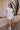 Full body view of model wearing the Sienna White Knit Mini Dress which features off white knit fabric with a monochrome block stripe design, mini length, two slit side pockets, a left front chest pocket, a round neckline and sleeveless.