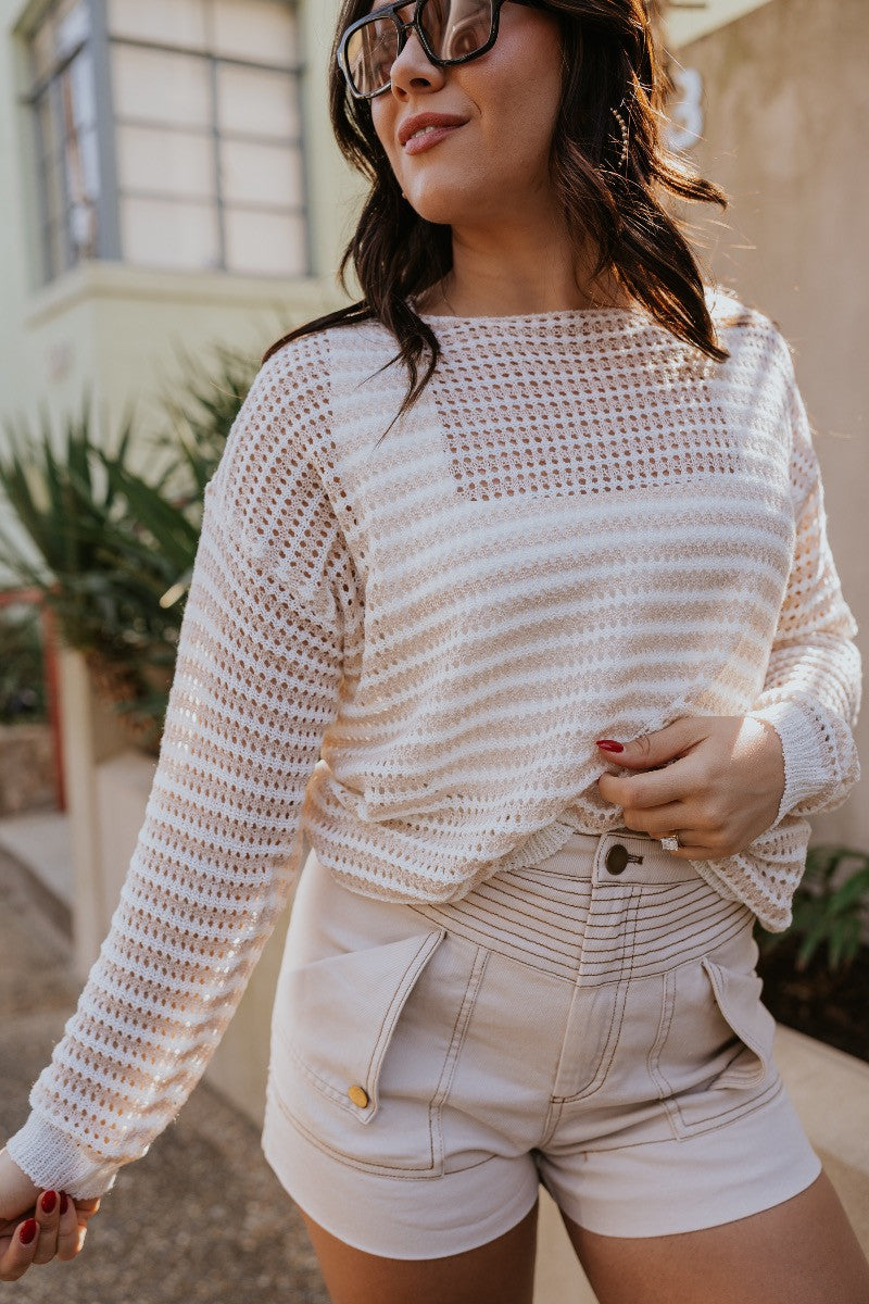 Front view of the Capri Knit Top which features white and tan open knit fabric, striped pattern, round neckline and long sleeves.