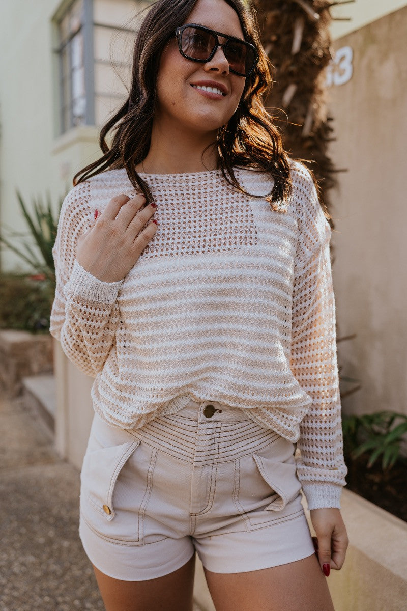 Front view of the Capri Knit Top which features white and tan open knit fabric, striped pattern, round neckline and long sleeves.