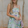 Front view of model wearing the Head Over Heels Floral Dress that has cream, blue, purple, green and light pink sheer floral fabric, a babydoll style, a square neck, spaghetti straps, an open back with a tied bow, and a back zipper closure