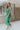 Side view of model wearing the Make You Mine Midi Dress that has green plisse fabric, a midi-length hem, a v neck, thick straps, a sleeveless body, and a back zipper with a hook closure.