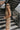 Side view of model wearing the Now Or Never Dress that has mocha ribbed fabric, a mini-length hem, a scoop neckline, adjustable double spaghetti straps, and a built-in bra