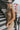 Close side view of model wearing the Now Or Never Dress that has mocha ribbed fabric, a mini-length hem, a scoop neckline, adjustable double spaghetti straps, and a built-in bra